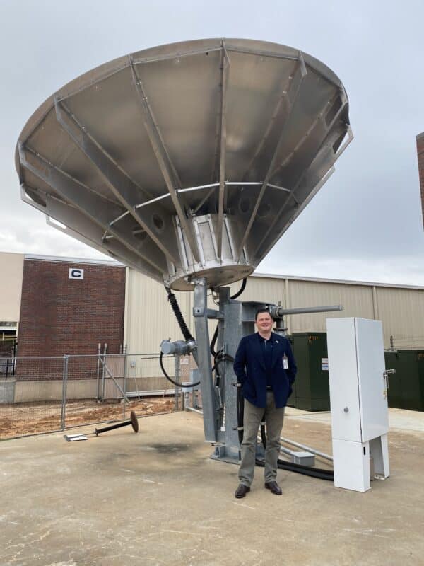 Michael Cratt standing in front of a satellite dish next to a building